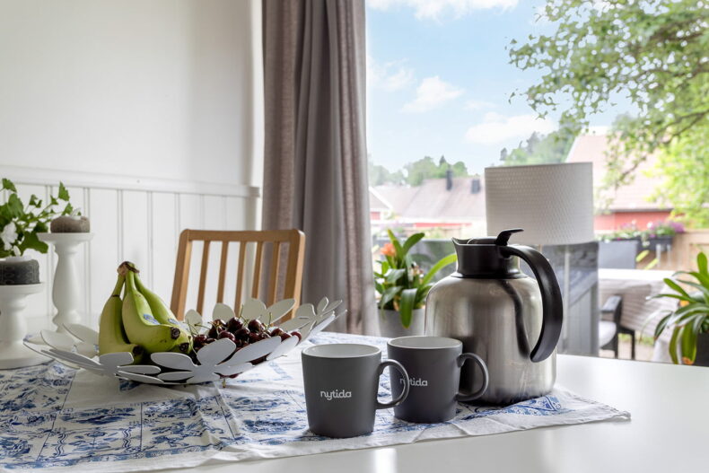 En närbild på ett bord med kaffetermos, muggar och en fruktskål.