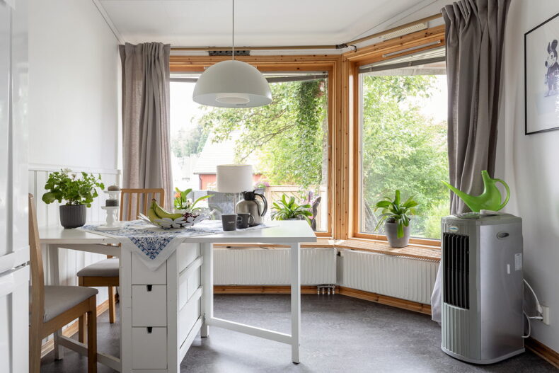 Vitt matbord intill stora fönster dekorerat med flertal växter