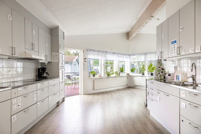 Boendets gemensamma kök med många ljusa fönster. På skåp och lådor sitter bildstöd för innehåll.