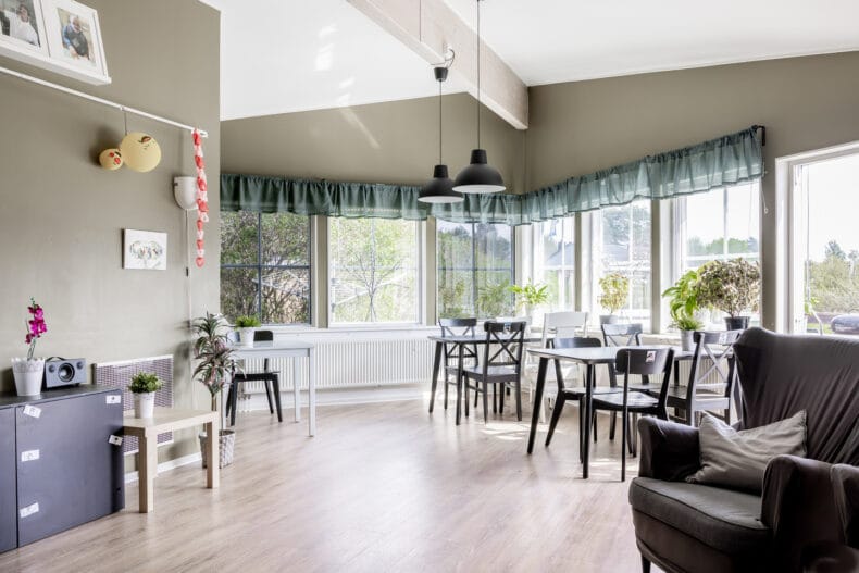 Boendets gemensamma del, med matbord, fåtölj och flera ljusa fönster