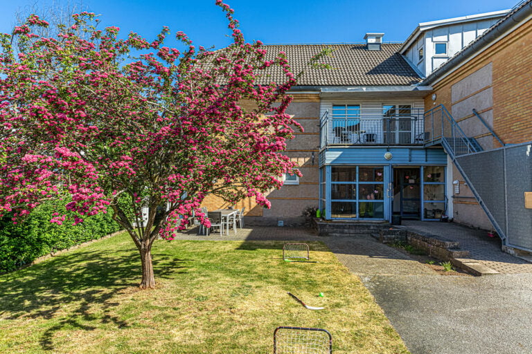 Boendets entré med uteplats och blommande träd på gräsmatta