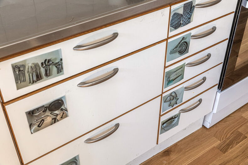 Närbild på gemensamma kökets lådor med bildstödtydligande bilder över vad som finns i varje låda i köket