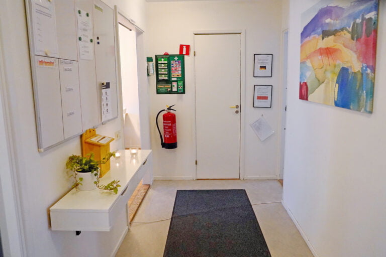 korridor, brandvarnare, förstahjälpen-kit vid dörr, svart matta, whiteboardschema