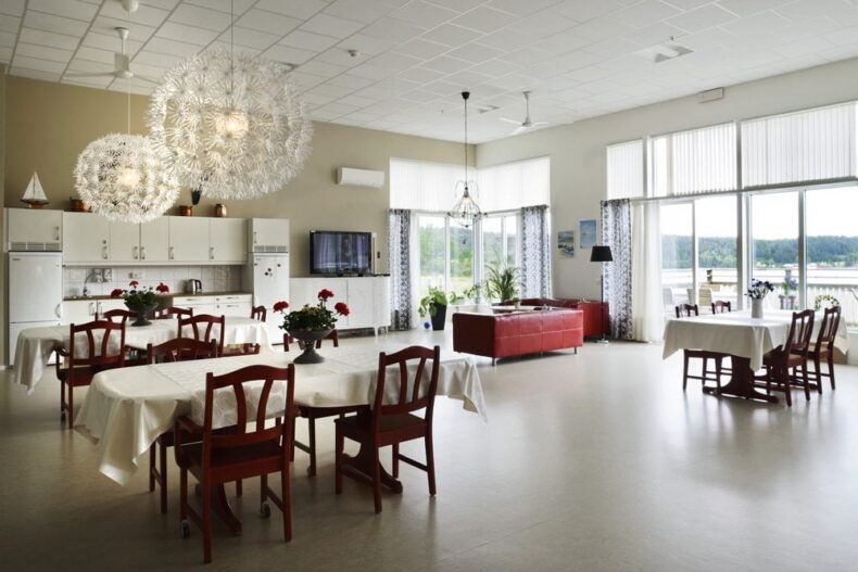 Boendets matsal med äldre möbler, linnedukar på borden och flera blomvaser