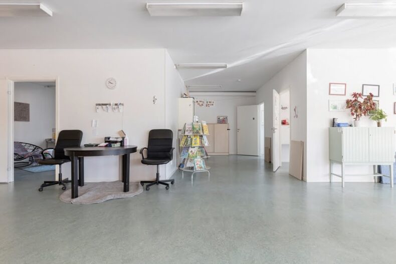 En öppen ljus yta med en bokställning och ett litet bord med två kontorsstolar