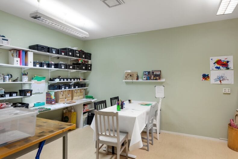 Ett pysselrum med två bord samt flera hyllor med lådor och material
