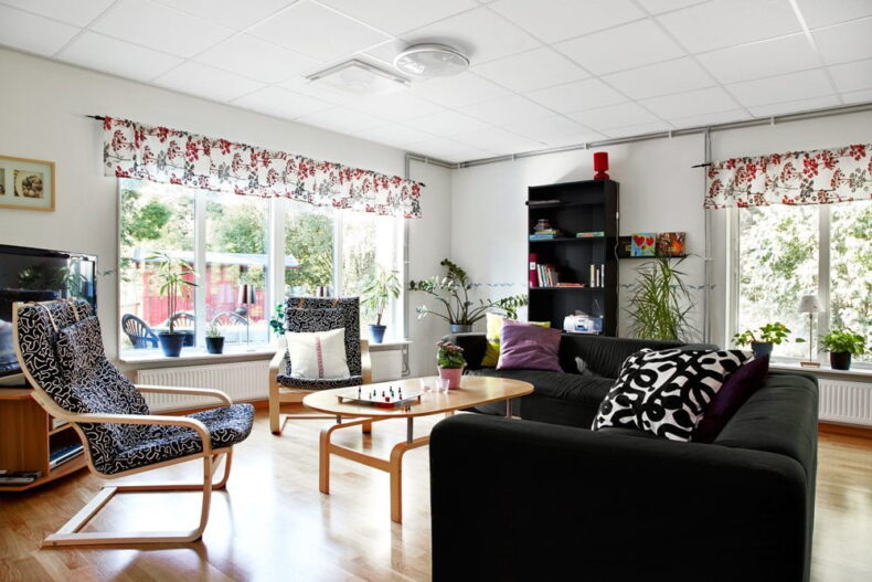 Boendets gemensamma del med soffa, fåtöljer, bokhylla och soffbord med ett brädspel framställt