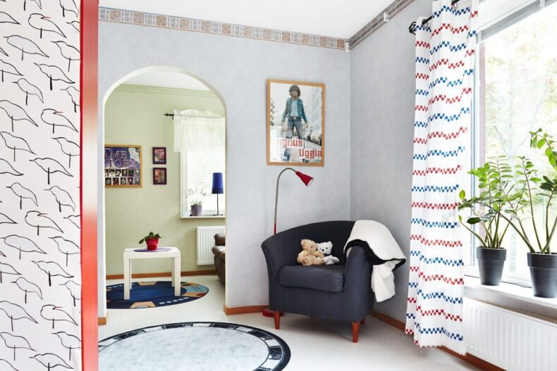 Ett mysigt hörn med en fåtölj vid ett dörrhål in till ett rum där det står en soffa och ett litet soffbord. I fönstren står krukväxter och på väggarna hänger flera tavlor