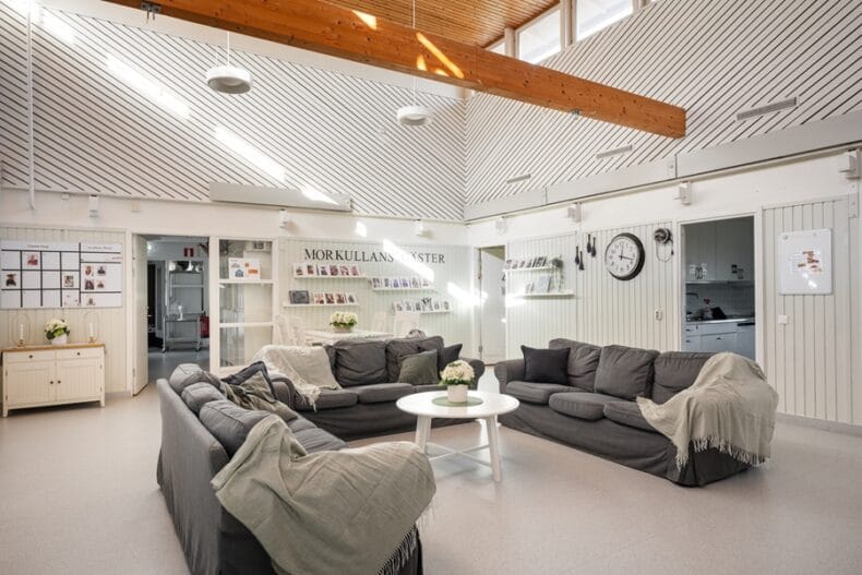 Ett mycket luftigt rum med väldigt högt i tak, där det står tre soffor kring ett soffbord närmast kameran och står ett bord med stolar längre bort. På väggarna hänger stora och små tavlor.