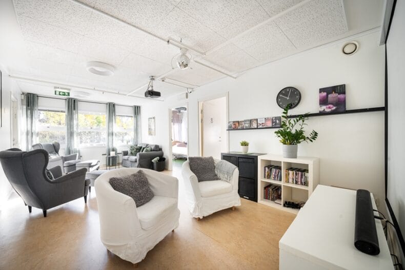 Ett TV-rum med flera fåtöljer och en liten bokhylla