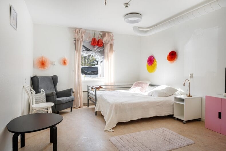 Ett större sovrum med en bred säng, en fåtölj, stol och soffbord