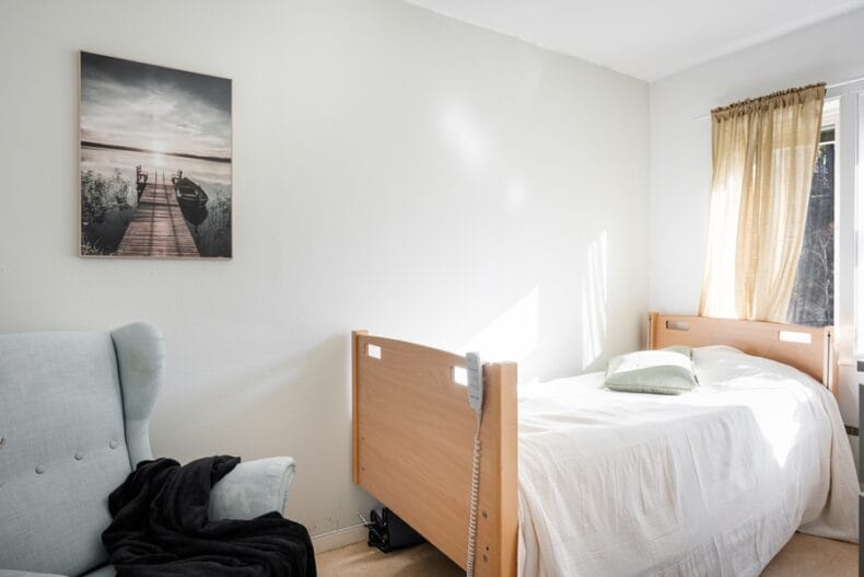 Ett av boendets sovrum inrett med justerbar säng, fåtölj samt en tavla