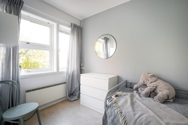 Ett av boendets sovrum inrett med säng, byrå och en stol. På sängen ligger en mjukis-elefant.