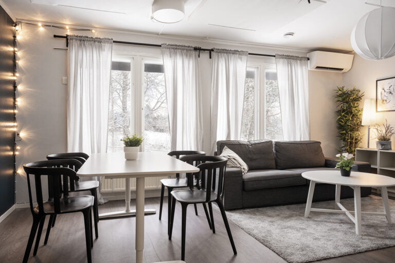 Gemensamt rum, grå soffa med vitt soffbord. Matplats. Stora fönster i bakgrunden