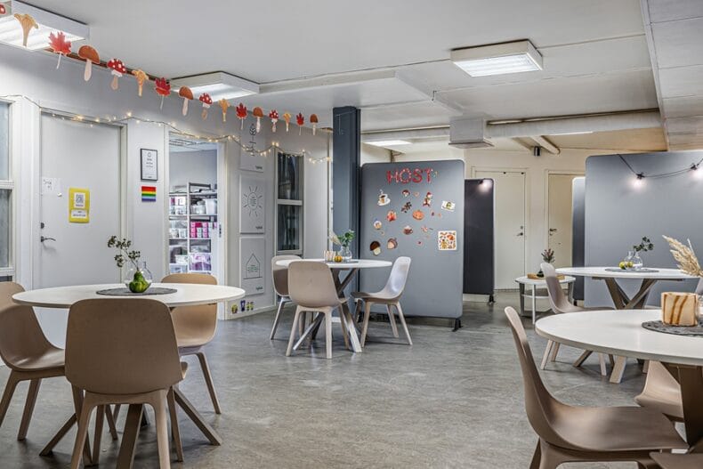 Verksamhetens matsal med runda bord och blå avdelnings-väggar med dekaler. I taket hänger en girlang av höstsvampar och löv i papper.