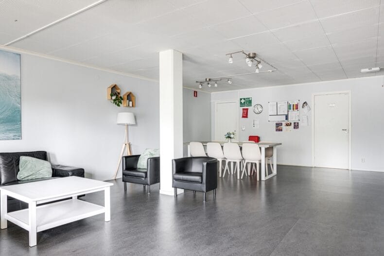 Stort gemensamt rum med soffa, fåtöljer och soffbord i förgrunden, matbord i bakgrunden