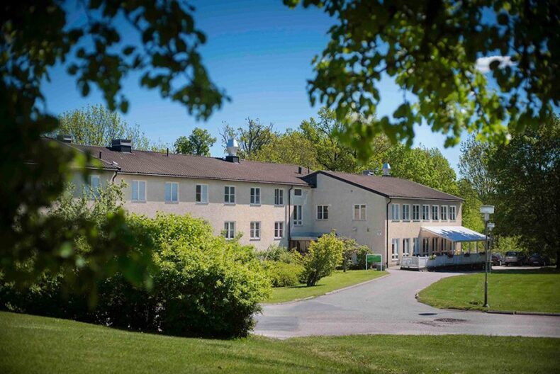 Boendets fasad sedd på håll, inramad av löv och grenar