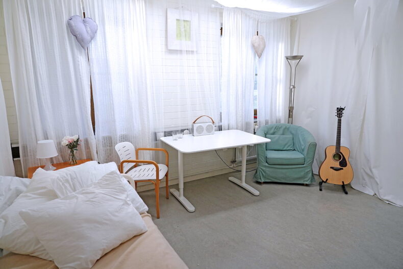 Ett rum med ljusa draperier på väggarna, soffa, skrivbord, fåtölj och en gitarr