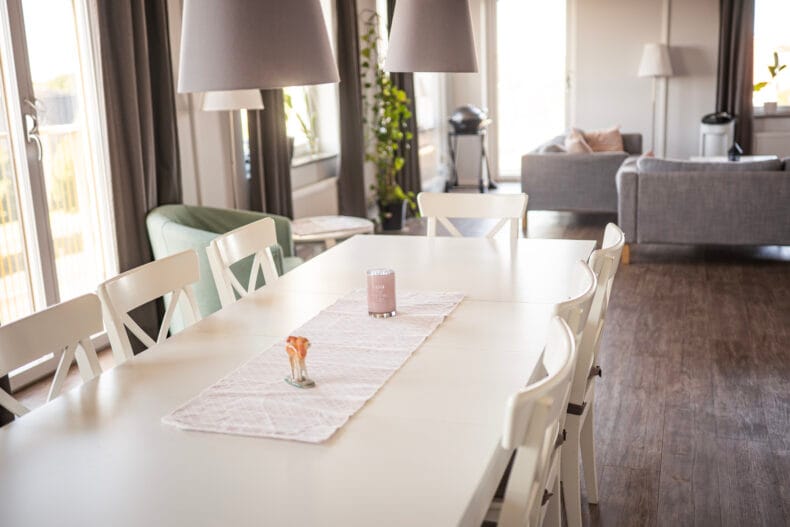 Vitt stort matbord med soffgrupp i bakgrunden och stora fönster till vänster.