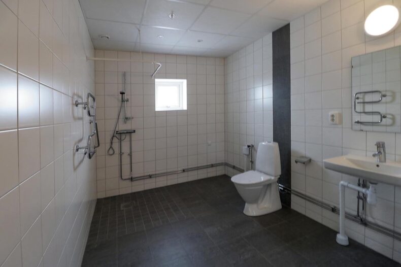 Badrummet i en av boendets lägenheter, med dusch, handukstork och stort handfat med spegel