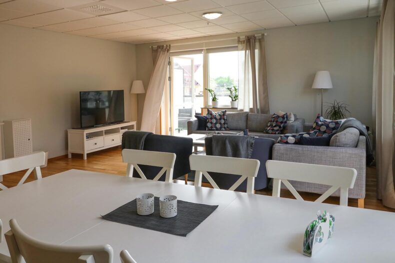 Boendets gemensamma ytor med matbord i förgrunden och en TV-hörna med soffor i bakgrunden