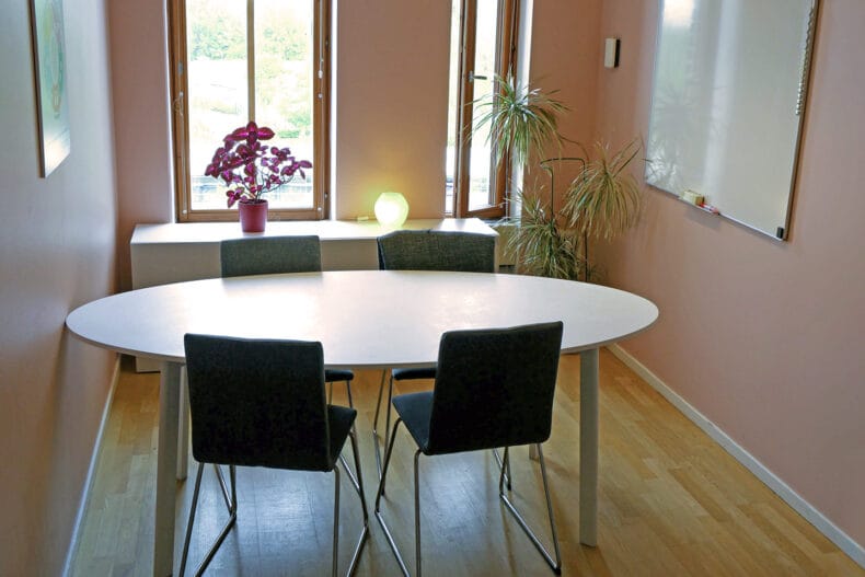 Litet rum med rosa väggar och ett ovalt vitt bord med gröna stolar