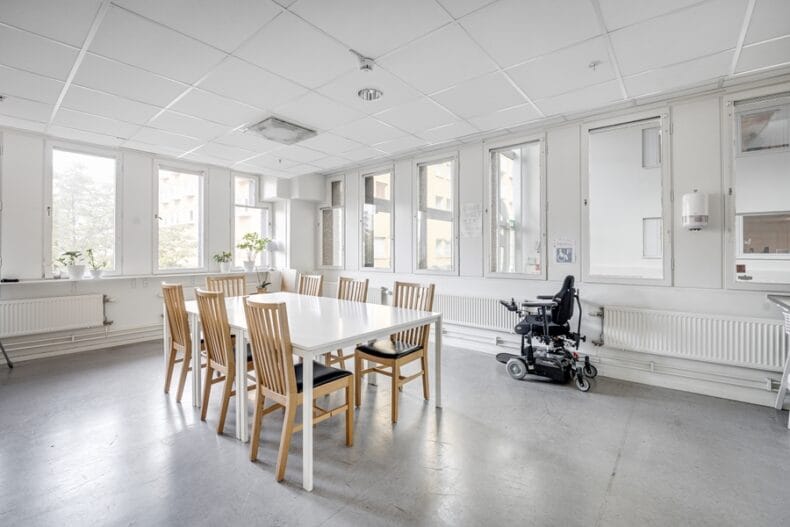 Stort luftigt rum med ett matbord. Vid ena väggen står en permobil.
