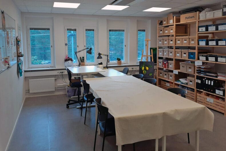 Rum med skrivbord och svarta stolar med bokhyllor med pysselmaterial