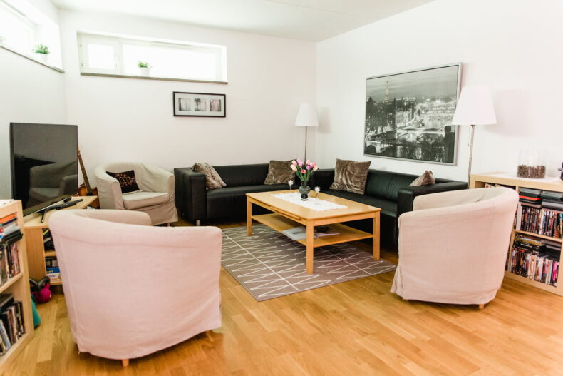 Gemensam TV-hörna med fåtöljer, soffor och bokhyllor. På väggarna hänger tavlor.