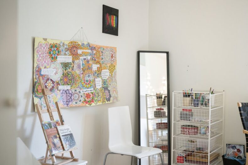 Ett rum med en golvspegel samt mycket material för målning. På väggen hänger ett collage av färglagda mandalas.