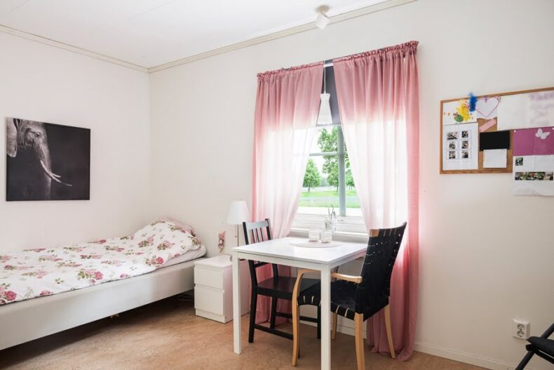 Ett sovrum med säng och nattduksbord samt ett litet bord med två stolar framför fönstret.