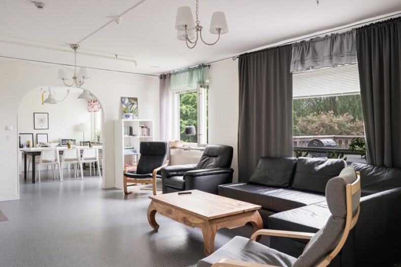 En gemensam yta med soffa och fåtöljer. Genom ett välvt dörrhål syns en matplats