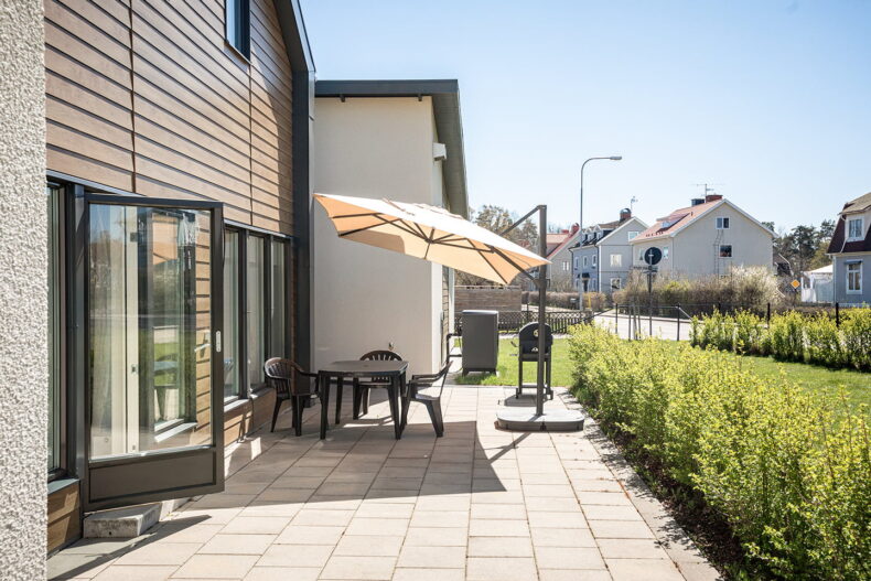 Boendets gemensamma uteplats med stenläggning, utemöbler och parasoll.