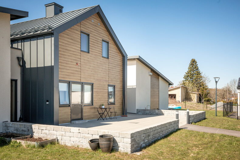 Boendets entré med stenlagd uteplats och en låg stenmur framför.