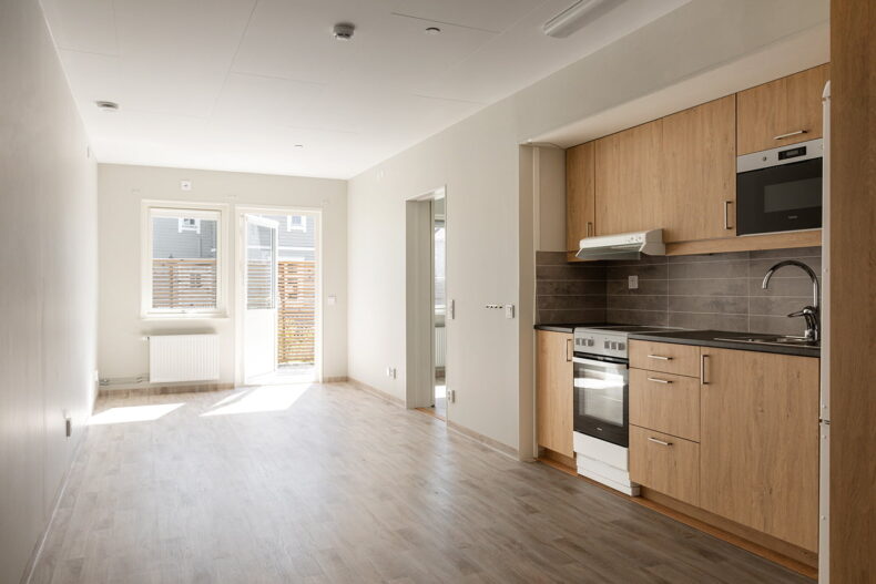 Ett omöblerat allrum med kök i en av boendets lägenheter. Längst bort är dörren öppen till en uteplats.