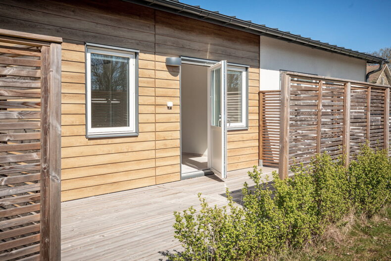 En uteplats med trädäck och spalje som ger insynsskydd till övriga lägenheters uteplatser.