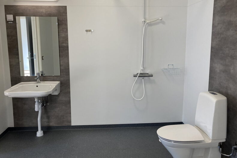 Badrummet i en av boendets lägenheter, med toalettstol, handfat med spegel, samt dusch.
