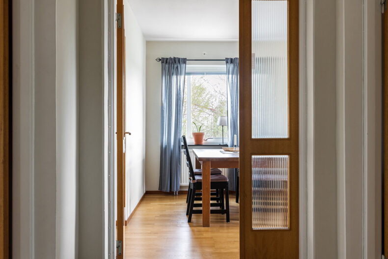 Ingång till vardagsrum. Stort fönster med blå gardiner i bakgrunden