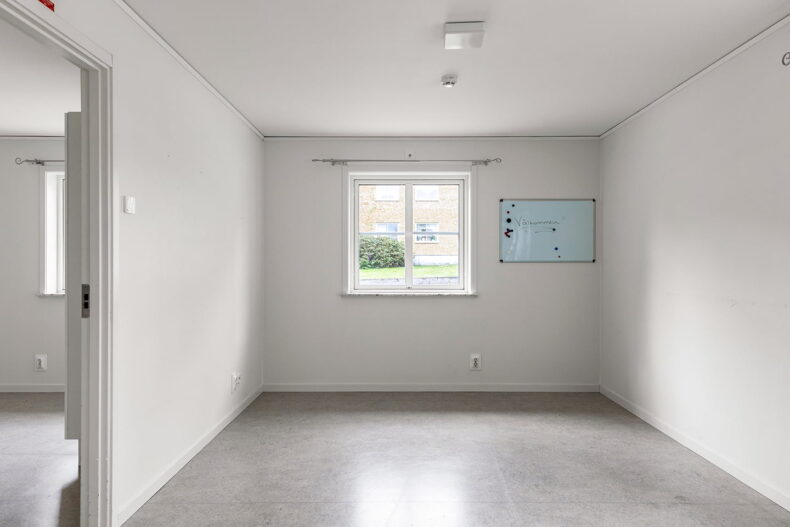 Ett omöblerat rum i en av boendets lägenheter. Bredvid fönstret hänger en whiteboard