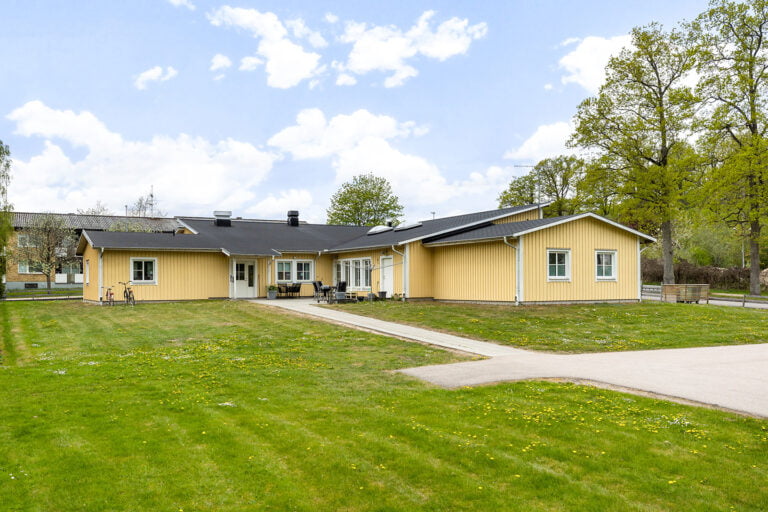 Boendets fasad med stenlagd gång och gräsmatta utanför