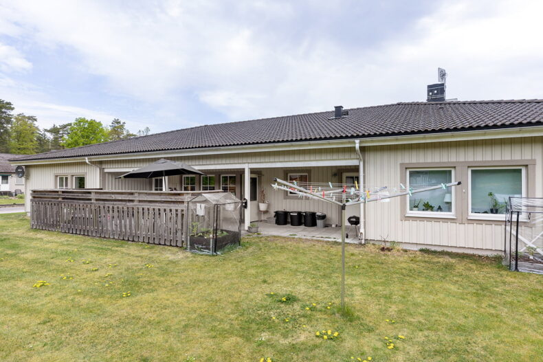 Boendets ljusa fasad och uteplats. På gräsmattan framför står en torkvinda.