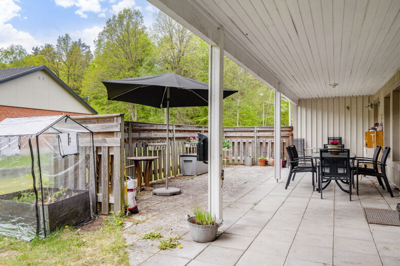 Uteplats med möbler, parasoll och odlingslåda.