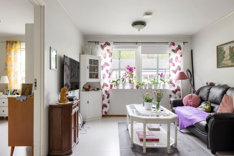 Hemtrevligt vardagsrum med soffa, TV och vitrinskåp. Dekorerat med rosa textiler