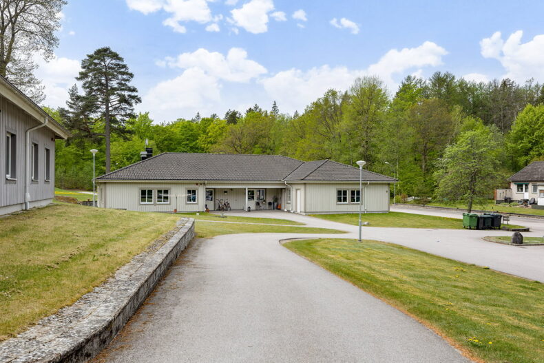 Boendets fasad, ett stort hus i ett plan, sett från bilvägen.