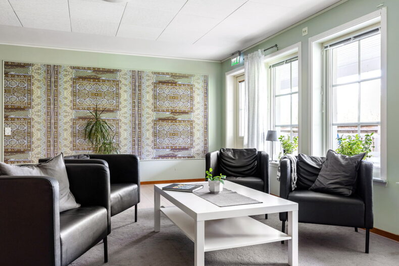 Gemensamt utrymme med svarta fåtöljer och stor tavla mot den ljusgröna väggen bakom