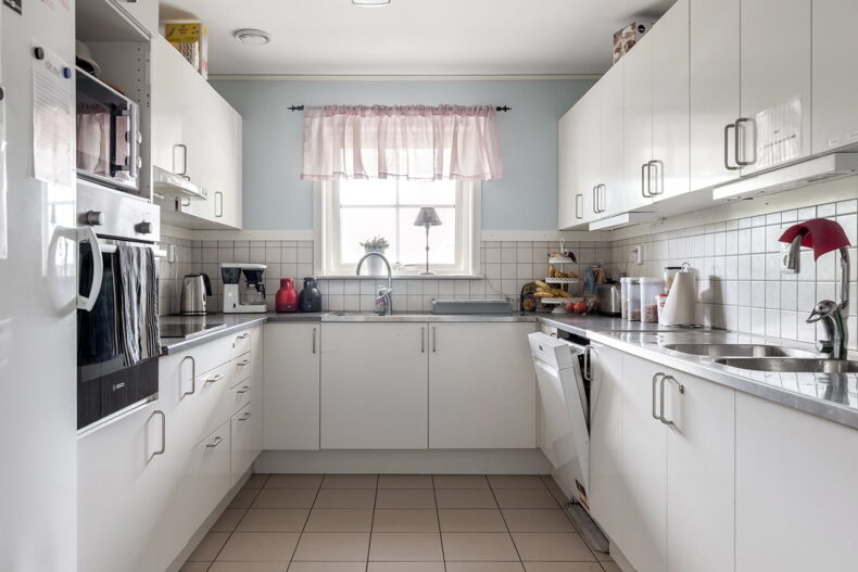 Gemensamt kök med vita köksluckor och vitt kakel