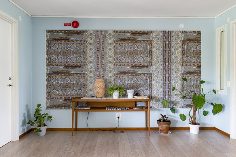Hörna med litet bord och flera krukväxter framför blåmönstrad vägg.