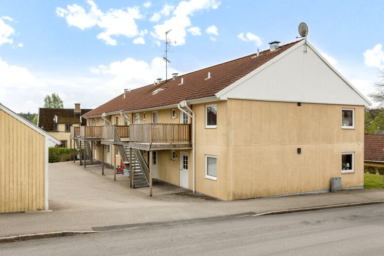 Servicebostadens gula tvåvåningshus med loftgång sett från bilvägen.
