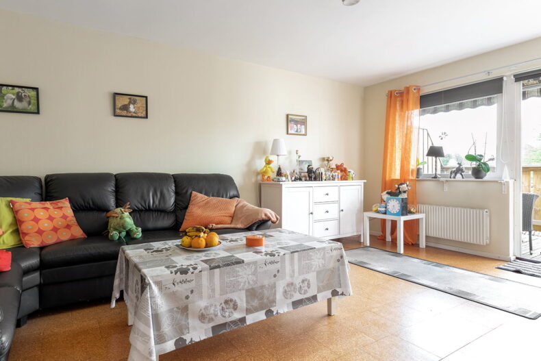 Vardagsrum med soffa, soffbord och byrå samt balkongdörr. Många gosedjur, prydnader och orange detaljer.