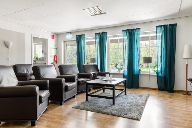 Gemensamt utrymme med läderfåtöljer och turkosa gardiner